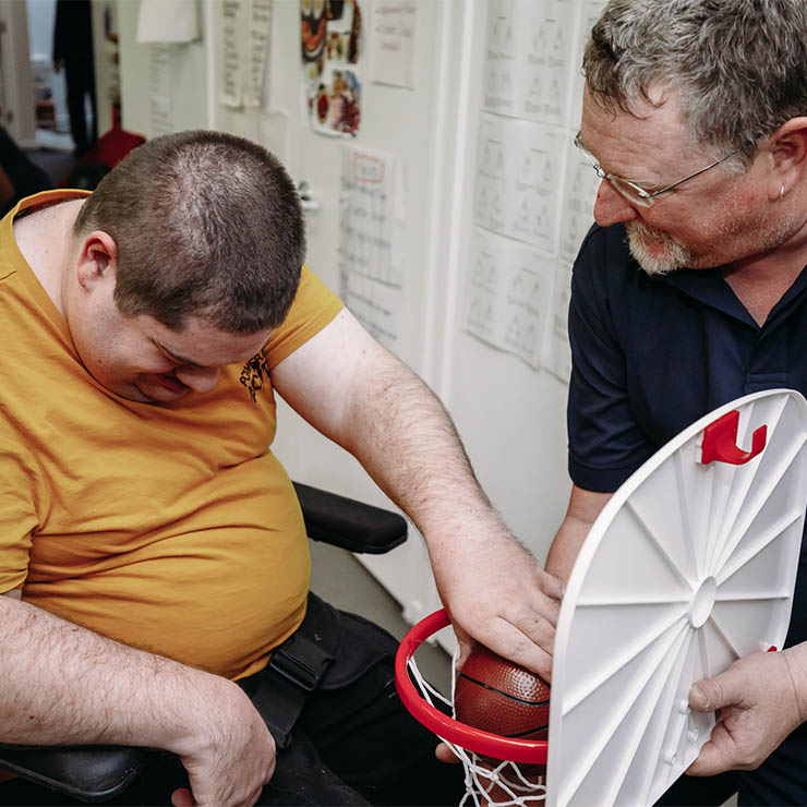 Waminda team member helping client put basketball in hoop